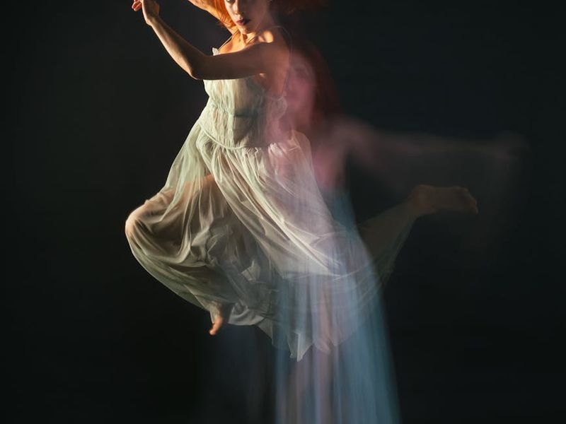 Person performing a fluid motion exercise in a minimalist dark room.